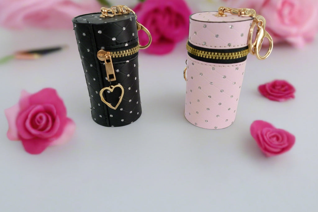 Two cylindrical jewelry cases, one black with gold accents and one pink with gold accents, on a white surface with pink flowers.