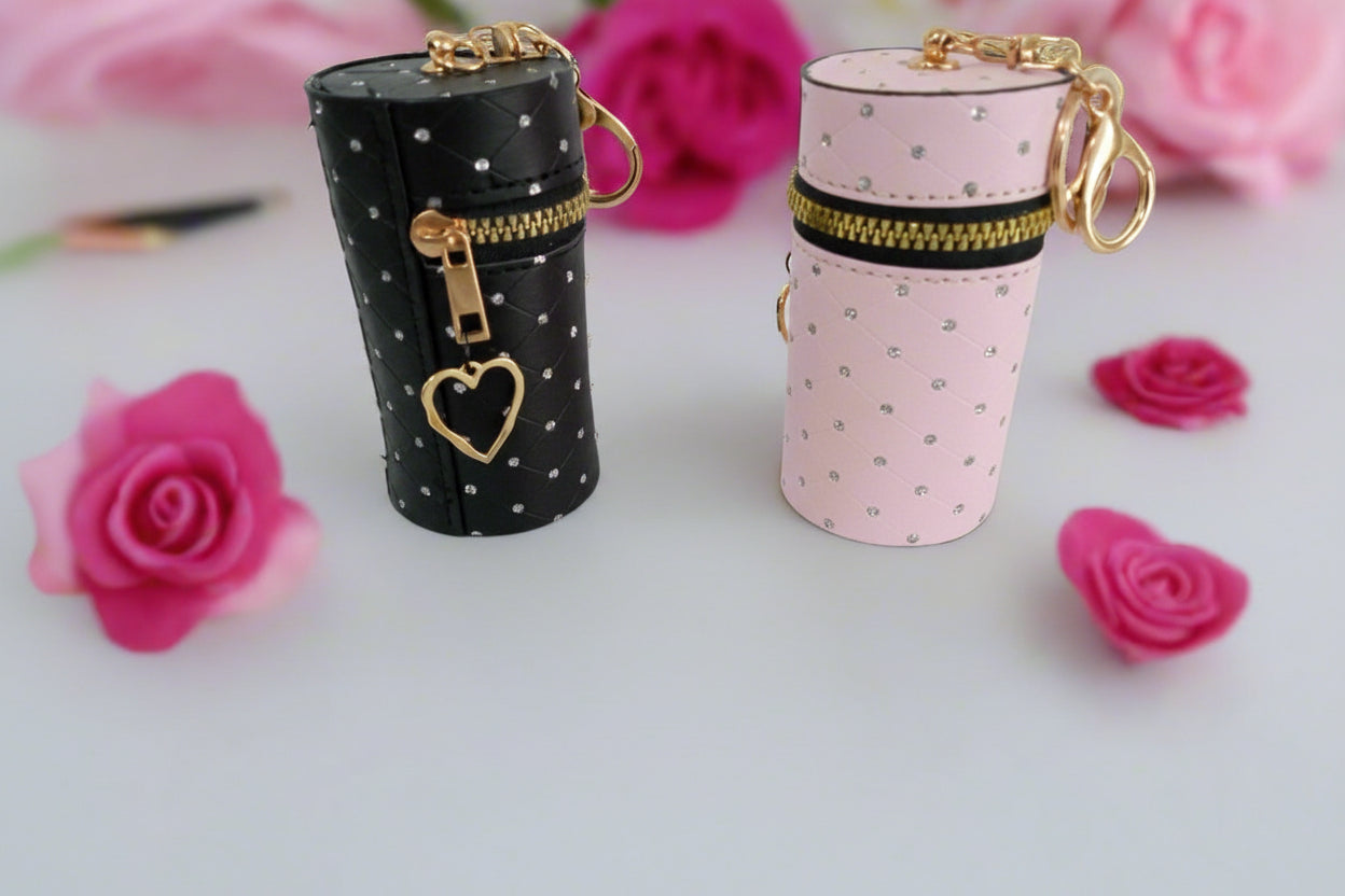 Two cylindrical jewelry cases, one black with gold accents and one pink with gold accents, on a white surface with pink flowers.