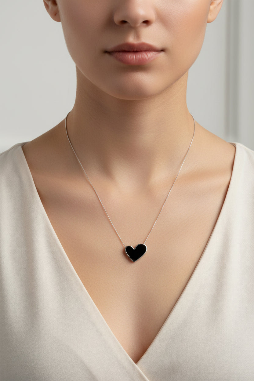 Black heart-shaped pendant on a silver chain against a white background